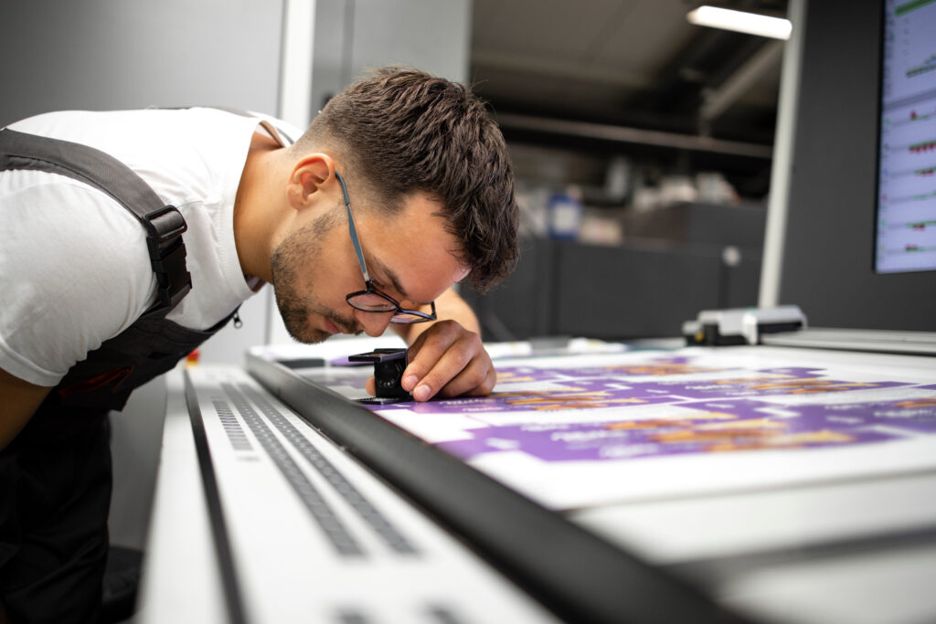 Worker checking print quality of graphics in modern printing hou